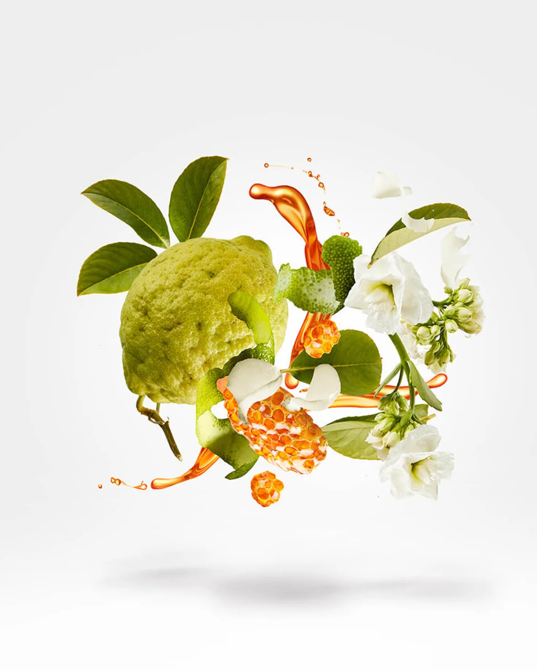 Green fruit with orange liquid and white flowers on a light gray background