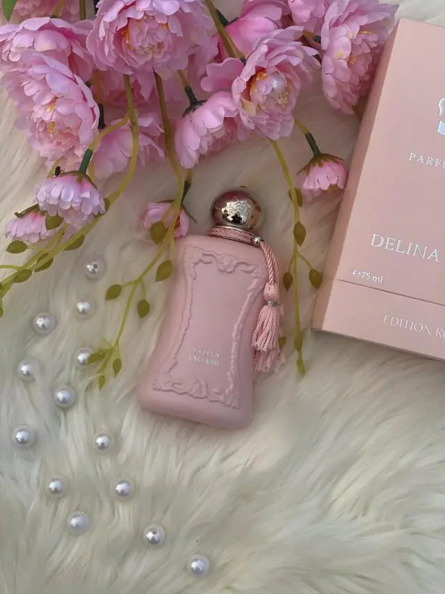 Pink perfume bottle with packaging and flowers on a textured surface