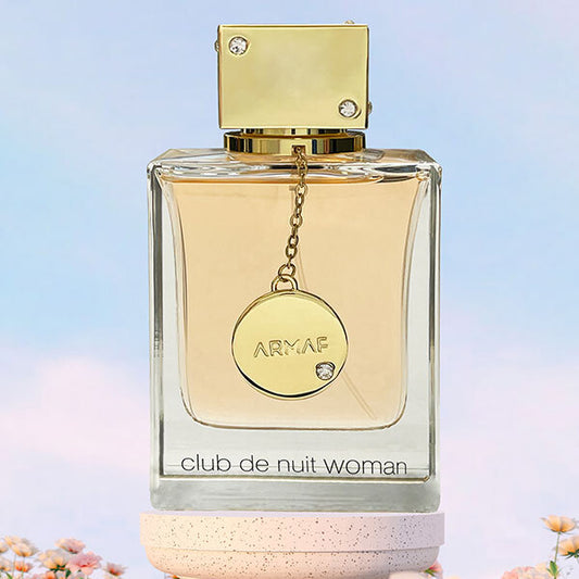 Perfume bottle labeled 'Armaf Club de Nuit Woman' with a gold cap and tag on a light blue background.