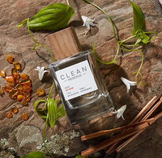 Clean Reserve perfume bottle on a stone surface with leaves and flowers