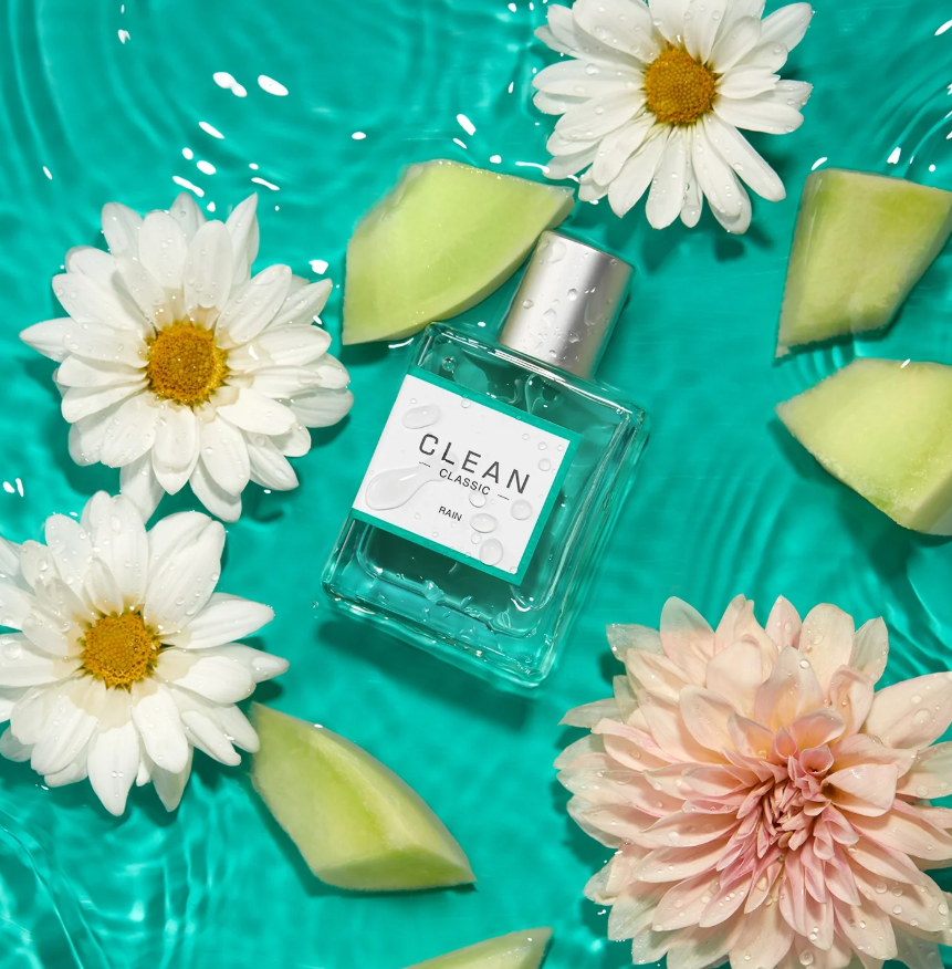 Clean perfume bottle with flowers and watermelon pieces on a teal background