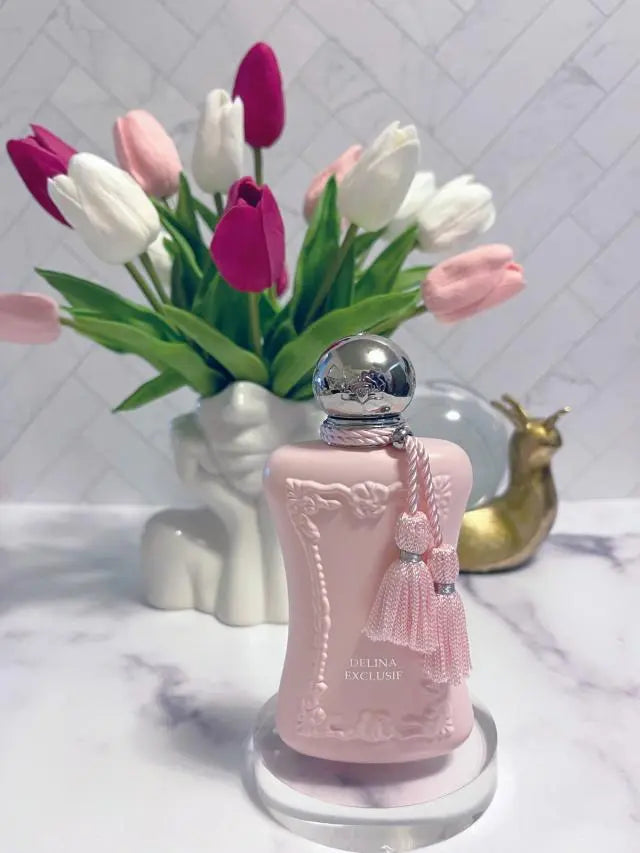 Pink perfume bottle with silver cap on a marble surface with tulips in the background