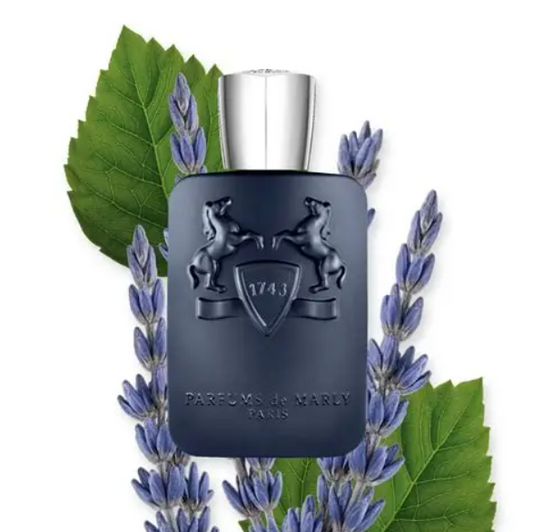 Dark blue perfume bottle with silver cap surrounded by lavender and green leaves on a white background