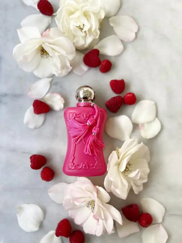 Pink perfume bottle surrounded by white flowers and red berries on a marble surface