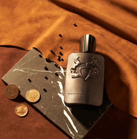 Silver perfume bottle with a lion emblem on a brown leather surface with coins.