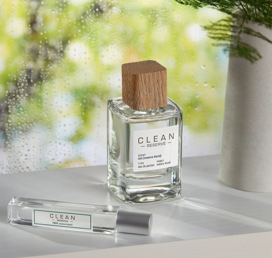 Clean Reserve perfume bottle with wooden cap on a reflective surface with a blurred green background