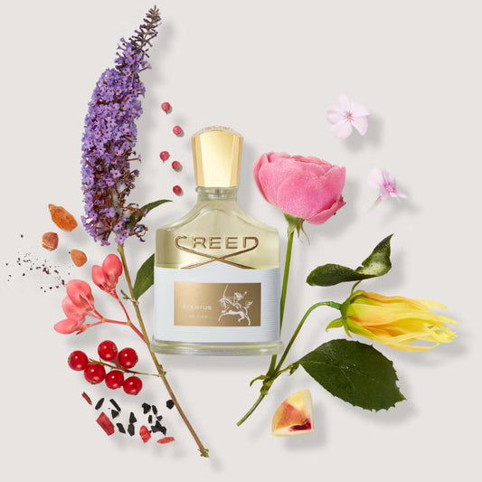 Creed perfume bottle surrounded by flowers on a light background