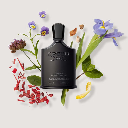 Black Creed perfume bottle surrounded by flowers and leaves on a light background